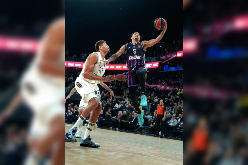 Action offensive d'un joueur du Paris Basketball s'envolant vers le panier sous la pression d'un défenseur du Real Madrid en EuroLeague.