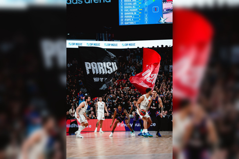 Phase de jeu entre le Paris Basketball et le Real Madrid avec de grands drapeaux brandis par le kop de supporters parisiens en arrière-plan.