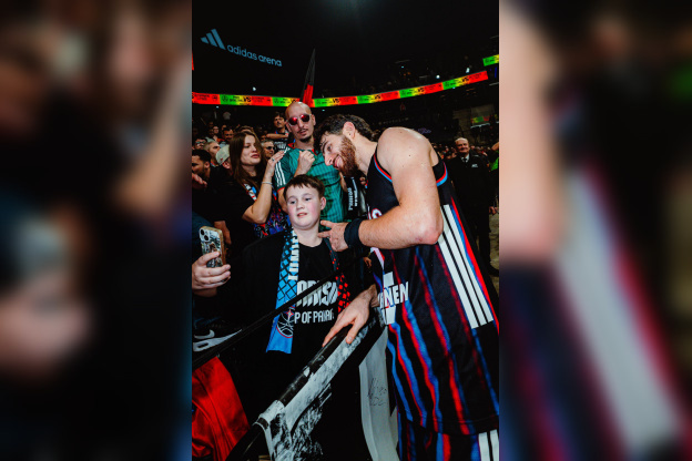 Un joueur du Paris Basketball prend un selfie avec des supporters dans les tribunes de l'Adidas Arena après un match.