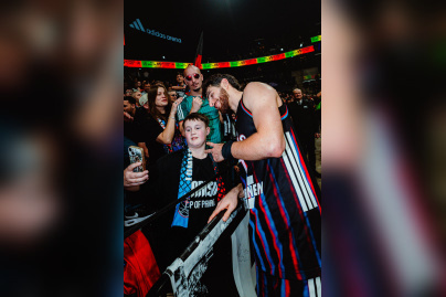 Un joueur du Paris Basketball prend un selfie avec des supporters dans les tribunes de l'Adidas Arena après un match.