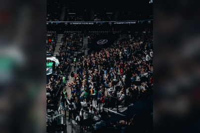 Vue d'ensemble des tribunes de l'Adidas Arena avec les supporters du Paris Basketball célébrant debout dans une ambiance électrique.
