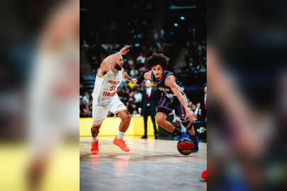 Joueur du Paris Basketball en pleine action offensive, dribblant face à un défenseur lors d'un match de basket intense.